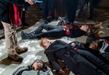 A foto mostra protestantes performance um "Die in". A manifestação é contra a família Sackler, ligado à Purdue Pharma, produtora do Oxy Contin. Em meio aos protestantes está a fotógrafa Nan Goldin, rodeada por papéis que dizem "Sackler Lie People Die" e frascos de remédio