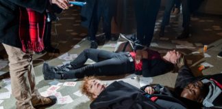 A foto mostra protestantes performance um "Die in". A manifestação é contra a família Sackler, ligado à Purdue Pharma, produtora do Oxy Contin. Em meio aos protestantes está a fotógrafa Nan Goldin, rodeada por papéis que dizem "Sackler Lie People Die" e frascos de remédio