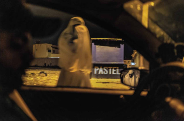 Na foto vemos uma das Alimentadeiras de Almas vestindo indumentária branca, a vemos pela janela de um carro, no reflexo do espelho do carro é possível encontrar uma segunda Alimentadeira. Atrás da primeira está uma banca azul escrito "pastel"