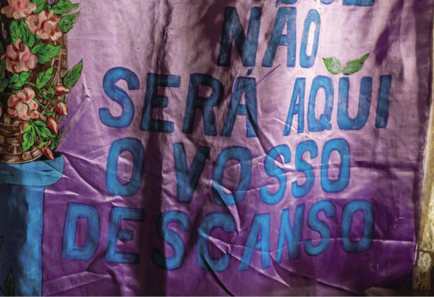 Manto pintado de roxo exibe em letras azuis a frase "Não será aqui o vosso descanso"