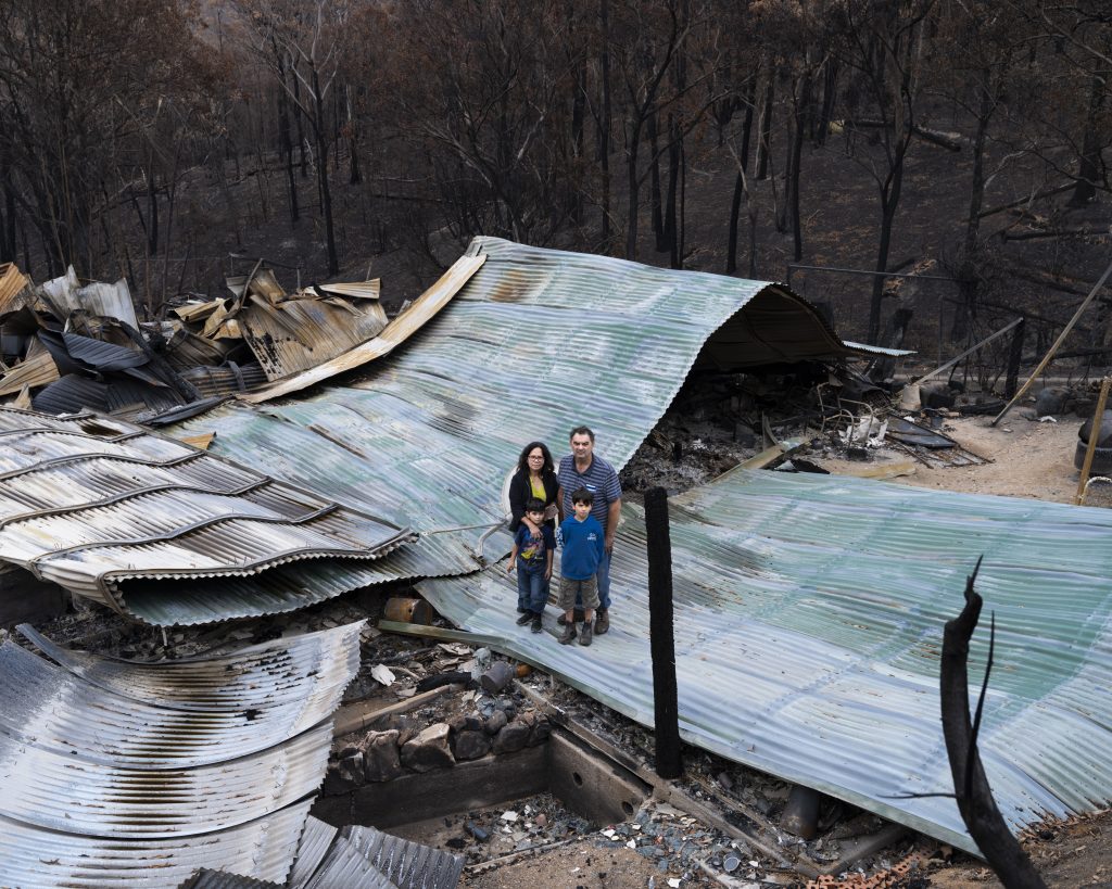 Gideon Mendel, série Fire, Anthony Montagner com sua família, sua esposa Fina e seus filhos Christian (9) e Dylan (6), onde costumava ser seu lar, agora completamente derrubado pelas chamas. Upper Brogo, Austrália, 18 de janeiro de 2020.