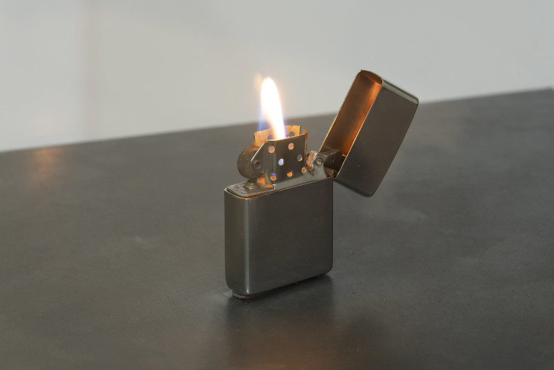 Imagem horizontal colorida. Isqueiro zippo aceso. Monumento virtual CHAMA, de Nuno Ramos, parte do projeto A EXTINÇÃO É PARA SEMPRE. 