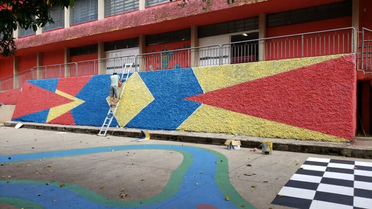 Foto horizontal, colorida. Coletivo Cicloartivo na EMEF Campos Salles criando um mural colorido e geométrico em uma das paredes da escola. A internvenção é parte do projeto Escola Criativa do Instituto Choque Cultural