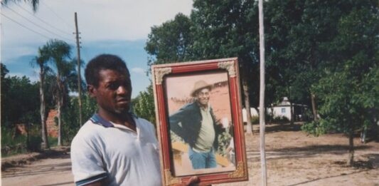 Seu Jovenil segurando o retrato do seu tio, Otávio Caetano, mestre da cupópia e festeiro da comunidade, sem data. Quilombo Cafundó, 35ª Bienal de São Paulo. Cortesia: CEDAE - Centro de Documentação Cultural Alexandre Eulálio, Universidade Estadual de Campinas